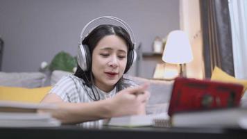 Asian girl wearing headset watching smartphone screen attending online class lesson inside home living room, video conference call from home distance education self study, e-learning study at home