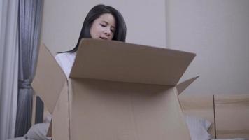 una joven asiática se sienta dentro del dormitorio y desempaca una caja de paquetes marrón, la mujer encontró cosas viejas dentro de la caja preguntándose qué es, el almacenamiento gestiona la reubicación, se queda en casa, abre la caja de entrega video
