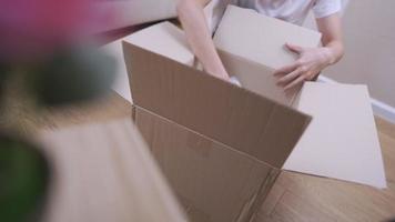 mujer joven empaca cosas en la caja de cartón del paquete, reubica la preparación, se muda, se sienta en el piso de la habitación, trabaja en la limpieza de la casa, organiza la crisis financiera del presupuesto voluntario, vive con sencillez video