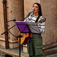 Modena, Italy, April 10, 2022, Female musician playing acoustic guitar and singing outdoor in the historic downtown district of Modena. Busking on street concept. Italy photo