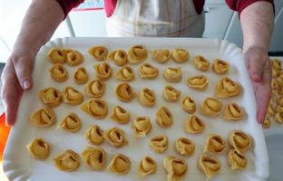 la cocinera italiana sostiene una bandeja de pasta tortellini en sus manos. foto