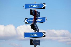 Road sign with names of capital cities isolated on blue sky background. London, New York, Rome, Paris, Rio, Berlin. photo
