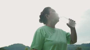 mulher asiática mais velha bebendo água de garrafa de plástico depois do trabalho no parque, refrescando o ar limpo e relaxante após o exercício, aposentado aposentado, vitalidade de bem-estar da saúde humana, reflexo do reflexo do sol