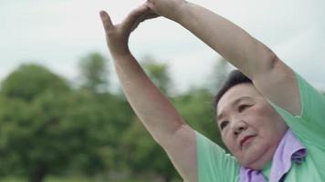 Asian active senior woman doing arm stretching warm up before exercise at the outdoor park, morning exercise routine, self-care motivation after retirement life, health care medical condition video