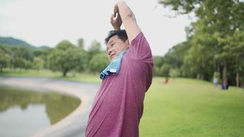 hombre maduro asiático haciendo estiramientos de brazos sobre la cabeza antes de hacer ejercicio en el parque al aire libre, rutina de ejercicio matutino, hombre activo de mediana edad, cuerpo jubilado más fuerte, estado de salud de los hombres, riesgo de cáncer