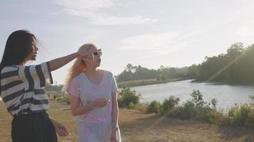 een modieuze vriendinnen die plezier hebben tijdens een wandeling langs een natuurlijke rivier in het nationale park, twee jonge toeristen die op zoek zijn naar een plek om te picknicken, beroemd zomerfestival, vrije tijd in de buitenlucht, jongeren video
