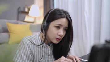 asiatisk ung kvinnlig kundtjänstpersonal bär headset pratar och skriver ner tangentbord, röstsamtal live interaktion med klient, online kundtjänst callcenter med personal, operatör som arbetar hemifrån video