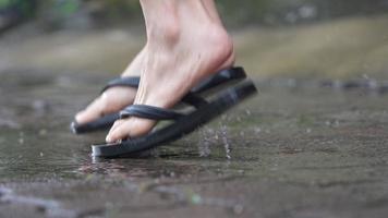 Low angle of a flipflops feet stomping playing on water puddle on the raining day,  flooding water on the street side, enjoying splashing dirty water, jumping goofy around, tropical raining season