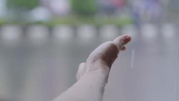 female hand reaching out her hand to feel the rain drops, Under Heavy Rain Close Up. Catches rains on Palm, rainy season in slow motion, with urban street background, touch nature, wet hand from rain video