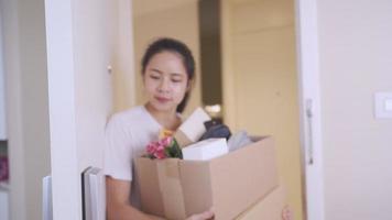mujer asiática adulta joven que ingresa al nuevo apartamento, lleva una caja de cartón marrón, deuda de préstamo de la casa, mudanza a un nuevo condominio, espacio de caja de almacenamiento en un nuevo lugar, estilo de vida de mujer soltera video