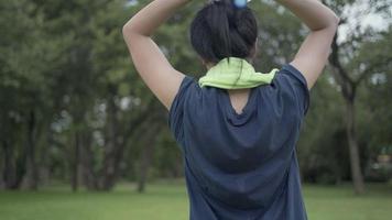 junge asiatische frau, die übungen auf einer frischen wiese vor einem natürlichen hintergrund ausdehnt, sich nach dem cardio-training am morgen zufrieden fühlt, den oberen rücken und die arme dehnt, das konzept, die lebenden menschen und die natur video