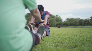 Asian senior couple stretching legs hand to toe sitting down on green grass public park, cool down after exercise family activities, retirement healthy life motivation, flexible body health condition video