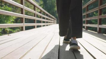 Young female in casual relaxing clothes with sneakers walking toward camera on the wooden bridge path way low angle, walking out the beginning of new chapter, step out of the comfort zone, taking risk video