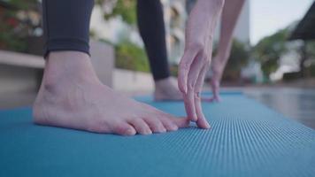 cierre la mano femenina alcanzando el pie practicando la pose de yoga inclinándose hacia el ejercicio de estiramiento, descalzo parado en la alfombra del piso, parte inferior del cuerpo flexible, alfombra de yoga, relajación corporal vitalidad de la salud, ángulo bajo