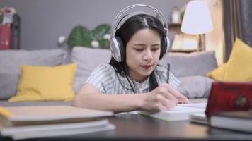 A serious female teaching freelancer works on lesson planning from home, reading textbook, sitting on cozy living room floor, using wireless headphone listen to online learning, distant internet job video