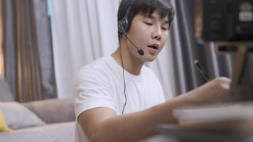 Asian young man in microphone headset, operator voice call interaction with customer, live chat, typing on the keyboard, social distancing doing work from home, home office during quarantine lockdown video