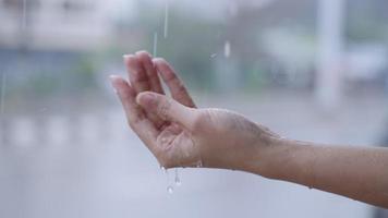 gotas de lluvia en la mano femenina de piel clara, día lluvioso con pase de conducción de automóviles en el fondo, bajo fuertes lluvias de cerca. atrapa lluvias en la palma, cámara lenta de la temporada de lluvias, de pie en el lado de la calle video