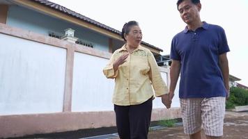 Asian senior couple walking together on village street with hands holding, relaxing exercise activity for elderly care, married lover arguing, reason explanation, family supporting each other, bonding