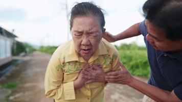 casal sênior relaxando andando em uma rua da vila quando uma idosa tendo um ataque cardíaco, mãos agarradas no peito, retrato de mulher idosa sofrendo de dores e marido preocupado com sua esposa