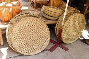 Rice winnowing basket or threshing basket are on floor beside bamboo table, another bamboo wicker are on table for sale in Thailand. photo