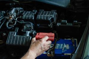 concepto de mantenimiento del motor. técnico está comprobando el nivel de energía de la batería. la mano de los hombres está examinando las principales fuentes de energía y los sistemas eléctricos de sus automóviles. la alimentación de CC falló. fondo borroso foto