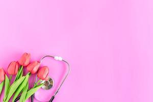 Happy nurse's day. Health day. Stethoscope, red tulips, on pink background. Greeting background. National doctor's day. Top view, Copy space on right. Thank you, doctors and nurses. Selective focus photo