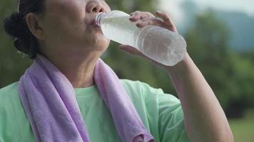 gros plan femme âgée asiatique boire de l'eau d'une bouteille en plastique après l'exercice au parc, activité de plein air relaxante après l'exercice, retraité actif optimiste, santé bien-être vitalité