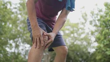 homme asiatique à la peau bronzée ayant une blessure douloureuse au genou pendant l'exercice de jogging à l'intérieur du parc avec des arbres en arrière-plan, état corporel douleur au genou, problème de ligament articulaire, exercice à l'extérieur mal au genou