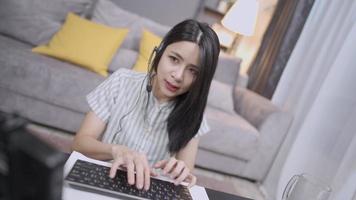 young Asian Female doing work from home as call center operator, online network connection, female wearing headset microphone, conference call with clients online distancing job recruitment online video