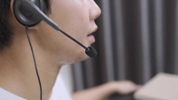 vue latérale homme asiatique tenant un microphone gros plan casque télé communiquant par appel en direct avec le client, bureau de travailleur à domicile, entretien d'embauche ou cours de langue en ligne à distance, parler avec le client