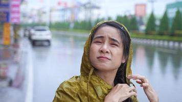 asiatisk flicka bär gul regnjacka på den regniga dagen står på vägkanten, regnperiod väder klimat hällregn, otur blir blöt när man går ut på jobbet, bil och motorcykel passerar förbi video