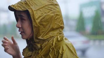 young pretty asian girl wear yellow raincoat standing on the road side, looking up to the sky enjoying the rain falling to her face smiling, rainy season weather climate pouring rain, feel fresh