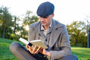 joven hipster masculino lee un libro en el parque de otoño foto