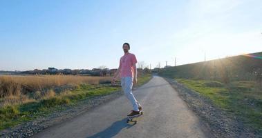 paseo masculino joven en patineta longboard en la carretera del país en un día soleado foto