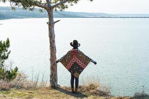 Yong hipster woman traveler in hat and poncho walking outdoors photo