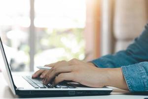 young man using laptop computer and mobile phone When looking for financial information in business, work at the desk. Writing with a pen, studying remotely from home and working from home. photo