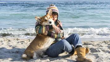 joven mujer feliz caminar con lindo perro corgi en la playa soleada de otoño foto