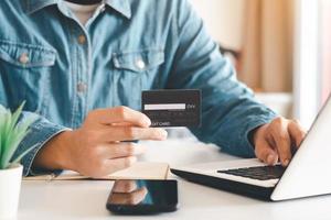 Businessman hand holding credit card with using laptop for online shopping while making orders at home. business, lifestyle, technology, ecommerce, digital banking and online payment concept. photo