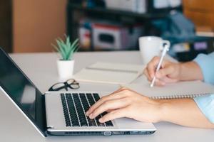 el hombre de negocios tomando notas resume la reunión en línea con una computadora portátil, trabajando solo, sentado en su escritorio. trabajando desde casa, manos de primer plano. foto