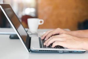 Close up shot of male hands typing on laptop while sitting at office desk indoors, man fingers tapping and texting on computer keyboard while working in cabinet, Work concept. photo