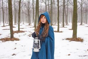 mujer joven con abrigo azul retro camina en el parque de niebla en invierno, fondo de nieve y árboles, concepto de fantasía o hada