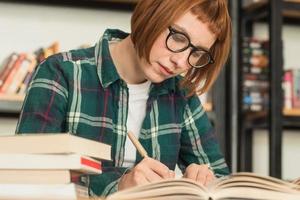 joven pelirroja con gafas lee un libro en la biblioteca foto