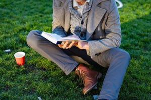 joven hipster masculino lee un libro en el parque de otoño foto