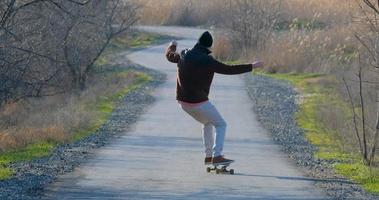 paseo masculino joven en patineta longboard en la carretera del país en un día soleado foto