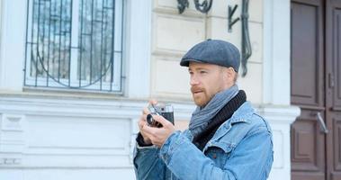 joven apuesto viajero masculino con cámara de cine hacer fotos callejeras
