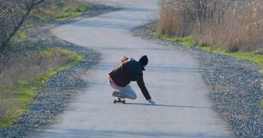 paseo masculino joven en patineta longboard en la carretera del país en un día soleado