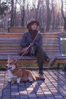 mujer joven con sombrero en el paseo por el parque con un lindo perro corgi, un día soleado de otoño foto