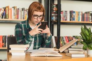 Young redhead woman in glasses read book in the library photo