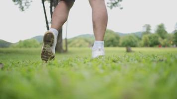 Aziatische mannelijke enkelrotatie warming-up oefening in het park lage hoek uitzicht op groen gras gazon, enkelpijn preventie, gewrichtsband probleem, onverwacht ongeval, benen kuitspieren pees strekken video