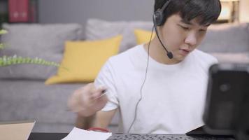 asiatische junge mam-arbeiterin trägt einen headset-anrufoperator, der sich notizen aus kundeninformationen macht, mikrofon-sprachanrufinteraktion mit kunden, live-chat mit mitarbeitern, soziale distanzierung bei der arbeit zu hause video